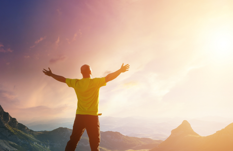 Man with outstretched arms looking out over mountains