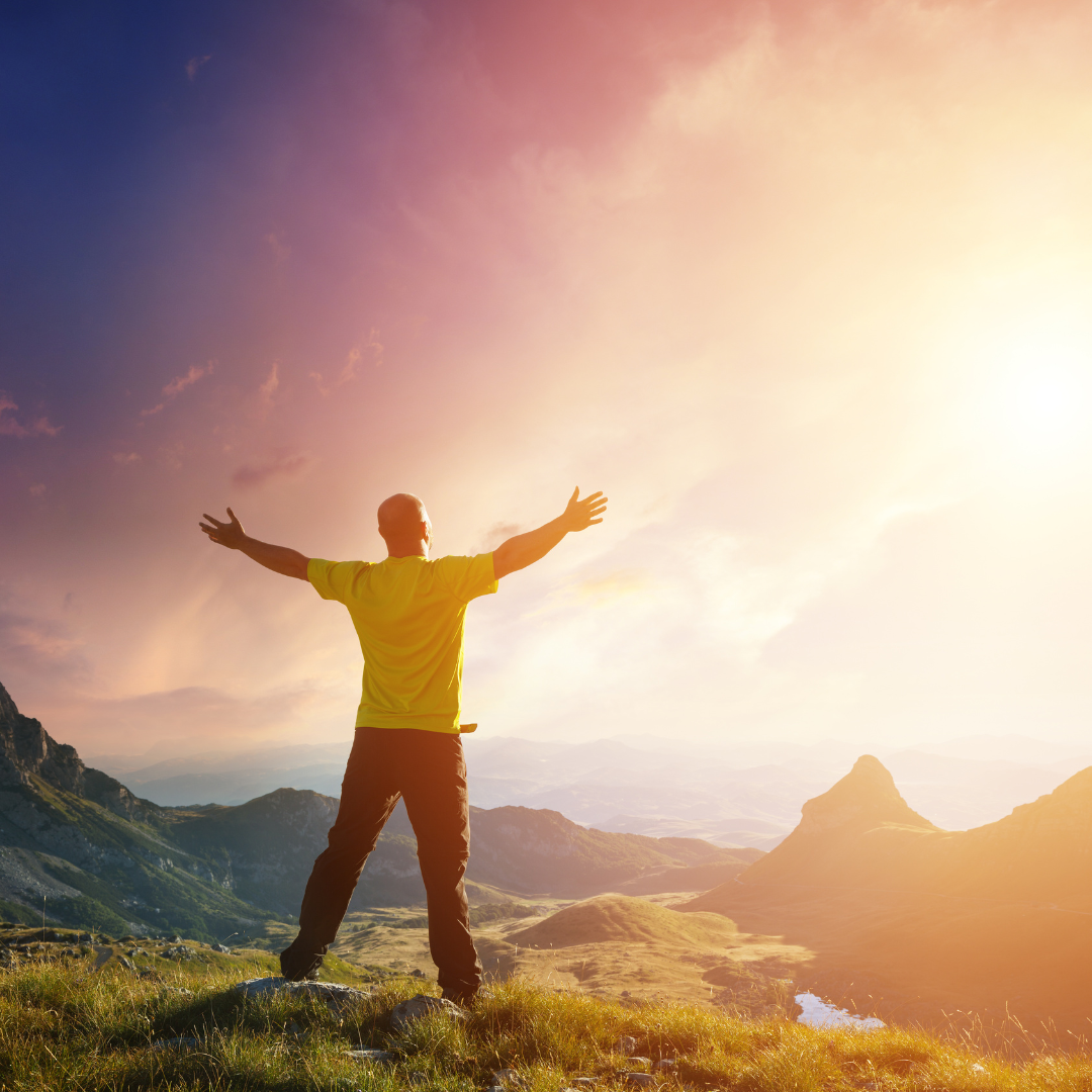 Man with outstretched arms looking out over mountains